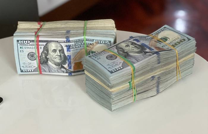 Picture of two stacks of $100 bills on a table each held together by rubber bands.